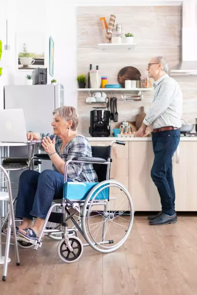 disabled-senior-woman-in-wheelchair-working-from-home-at-laptop-in-kitchen-682x1024